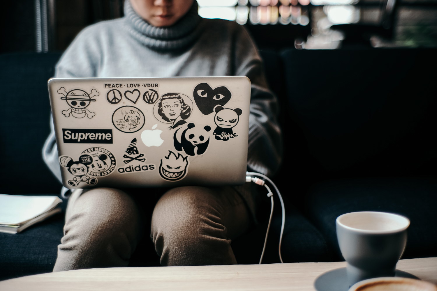 person sitting using sticker-covered macbook with mug on table